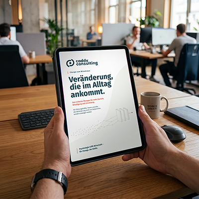 Hände, die Tablet mit Toolkit Cover halten, im Hintergrund arbeiten drei Männer am Rechner